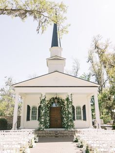 an outdoor wedding venue with white chairs and greenery on the front door, surrounded by trees