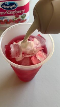 someone is pouring ice into a cup filled with red liquid