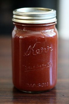 a jar filled with ketchup sitting on top of a wooden table next to a spoon