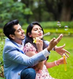 a man and woman sitting on the ground blowing bubbles in front of them with their hands