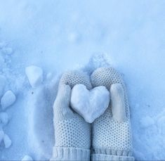 a person's hands in mittens holding a heart shaped snowball on top of the snow