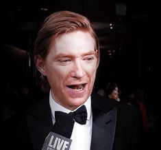 a man in a tuxedo is making a funny face while holding a microphone