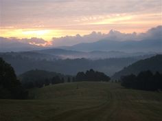 the sun is setting over some hills and trees