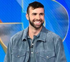 a man with a goatee smiles while standing in front of a blue background and smiling