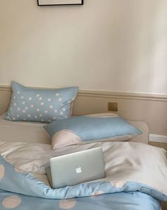 a laptop computer sitting on top of a bed with blue sheets and polka dot pillows