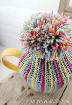 a crocheted tea cosy sitting on top of a wooden table next to a cup