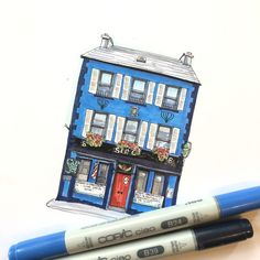 two markers are next to a drawing of a blue building with windows and shutters