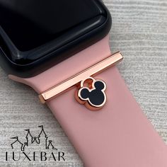 a pink apple watch with a mickey mouse pin on it's side and an iphone in the background