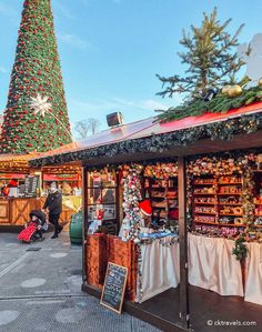 an outdoor christmas market with a large tree in the background