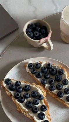 two pieces of toast with blueberries and cream on them next to a cup of coffee