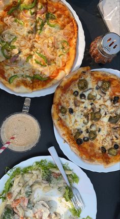 three pizzas and salad on plates sitting on a table with utensils in front of them