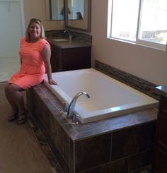 a woman sitting on the edge of a bathtub in a bathroom with tile flooring