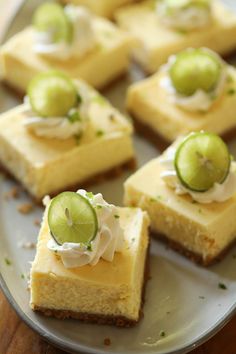 small squares of cheesecake with limes and whipped cream on top, sitting on a plate