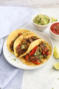 two tacos on a plate with salsa and guacamole next to it