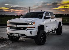 a white truck parked in a parking lot with the sun going down on it's horizon