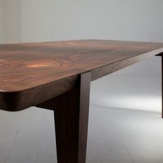 a wooden table sitting on top of a white floor next to a chair and wall