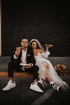 a bride and groom sitting on the ground eating pizza