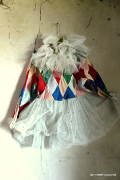 there is a dress hanging on the wall and it has many different colored ribbons around it