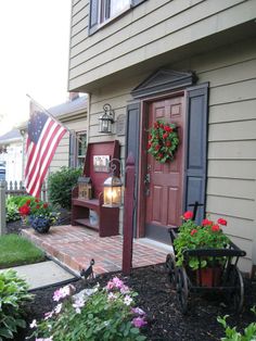 an american flag hanging on the side of a house next to some flowers and potted plants