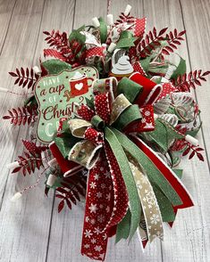 a christmas wreath on top of a wooden table with red and green ribbons, bows and decorations