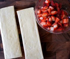 two pieces of bread sitting on top of a wooden cutting board next to a bowl of strawberries