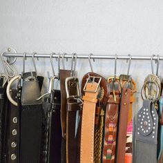 there are many different belts hanging on the rack in front of the wall and one is empty