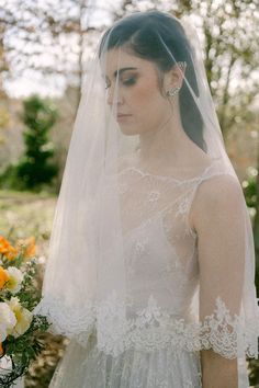 a woman in a wedding dress with a veil over her head and flowers behind her