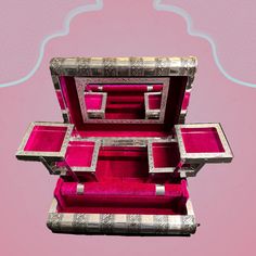 an open jewelry box with pink velvet linings and silver trim on the inside, against a light pink background