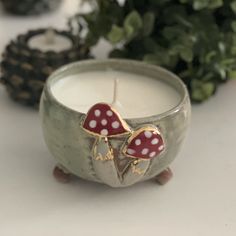 a candle with two hearts on it sitting in front of some plants and pine cones