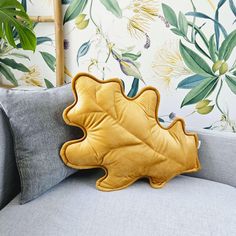 a yellow leaf shaped pillow sitting on top of a gray couch next to a green plant