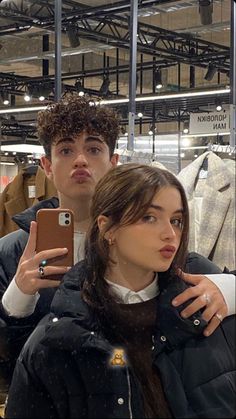 a man and woman taking a selfie in a clothing store with their cell phones