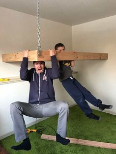 two men are hanging upside down on wooden planks in a room with green carpet