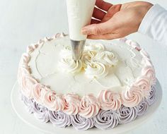 a person is decorating a cake with white frosting and pink flowers on it