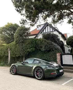 a dark green sports car parked in front of a house with trees and bushes behind it