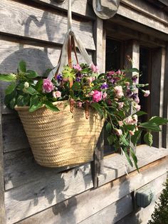 a basket filled with flowers hanging from the side of a wooden house window sill