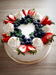 a white cake topped with berries and blueberries on top of a wooden table next to a knife