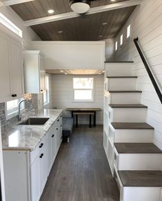 a kitchen and stairs in a tiny home with white walls, wood flooring and cabinets