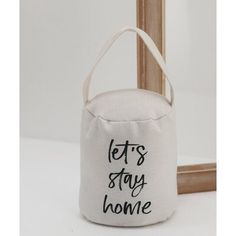 a white canvas bag with the words let's stay home printed on it, hanging from a wooden frame