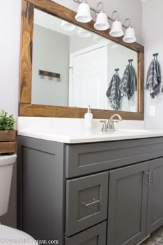 a bathroom with gray cabinets and white counter tops is pictured in this image, there are three lights on the mirror above the sink