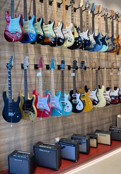 guitars and amps are lined up on the wall in front of eachother