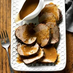 a white plate topped with meat covered in gravy next to a knife and fork