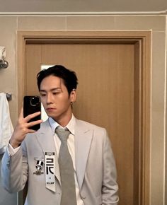 a man in a suit and tie taking a selfie with his cell phone while standing in front of a bathroom mirror