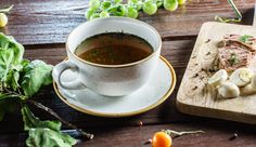 a cup of soup on a wooden table next to some vegetables and meats,