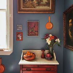 a kitchen with blue walls and pictures on the wall, including oranges in a bowl