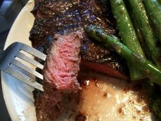 a piece of steak and asparagus on a white plate with a silver fork