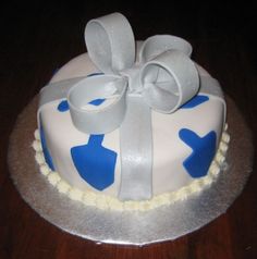 a white and blue decorated cake with a bow on it's top sitting on a wooden table