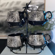 four black and white coffee mugs with spider web designs on them sitting on a metal stand