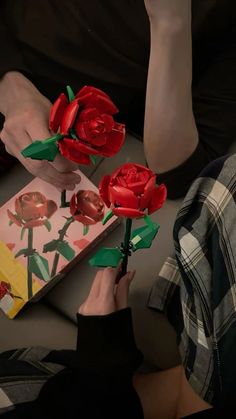 a person holding two red roses in front of a card with the same design on it