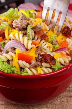 a red bowl filled with pasta salad and a fork sticking out of the top one