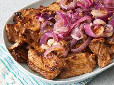 a white plate topped with meat and onions on top of a blue and white table cloth